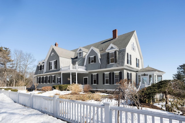 view of front of house with a chimney, a shingled roof, a gambrel roof, fence, and a balcony