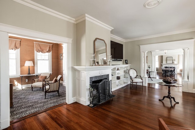 interior space with crown molding, wood finished floors, a fireplace with flush hearth, and ornate columns