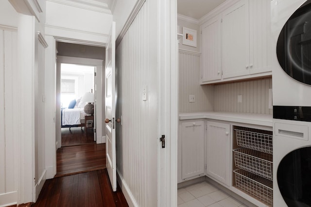 laundry room with cabinet space, light wood-style flooring, crown molding, and stacked washer / drying machine