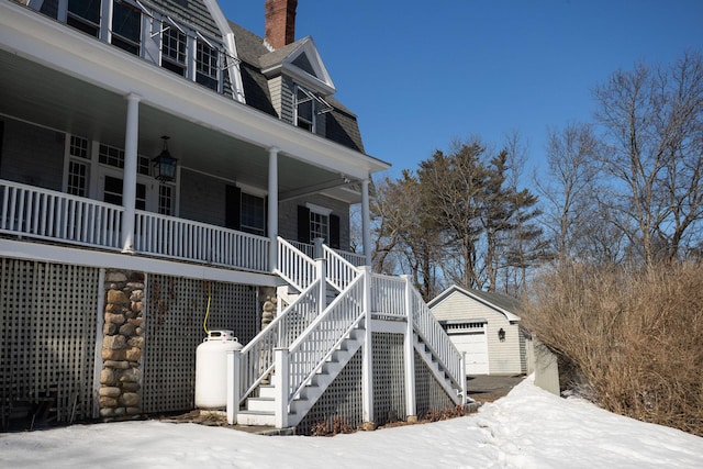 view of snowy exterior featuring a garage, covered porch, an outdoor structure, and stairs