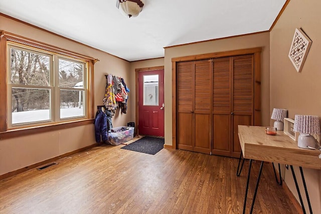 foyer with ornamental molding, wood finished floors, visible vents, and baseboards