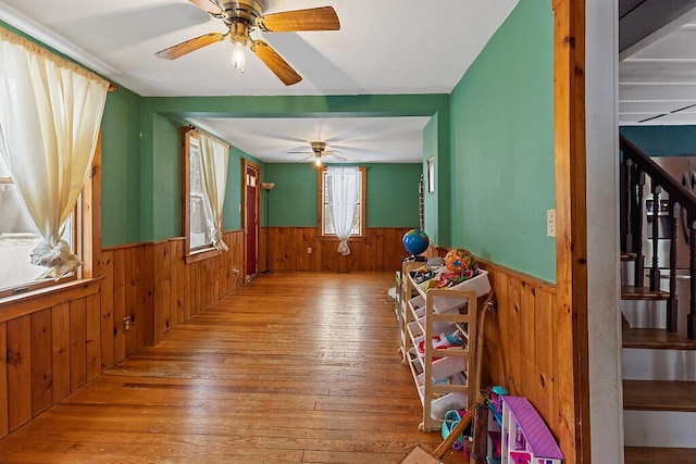 interior space featuring a ceiling fan, wood-type flooring, a wainscoted wall, and wood walls