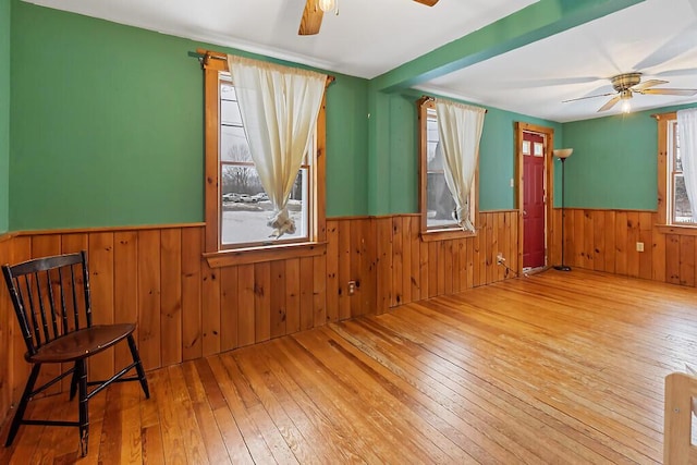 unfurnished room with a healthy amount of sunlight, a wainscoted wall, ceiling fan, and wood-type flooring