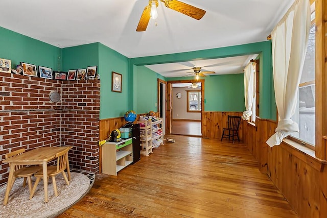 game room with a wainscoted wall, wood-type flooring, a ceiling fan, and wooden walls