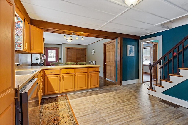 kitchen with light countertops, a sink, dishwasher, a peninsula, and baseboards