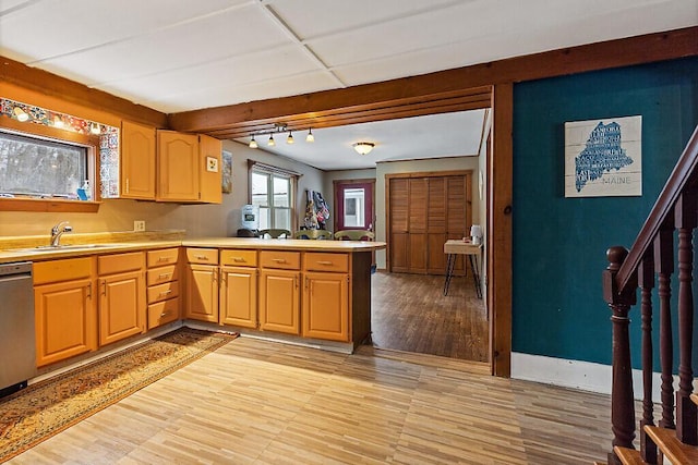 kitchen with light wood-style flooring, a peninsula, a sink, light countertops, and stainless steel dishwasher