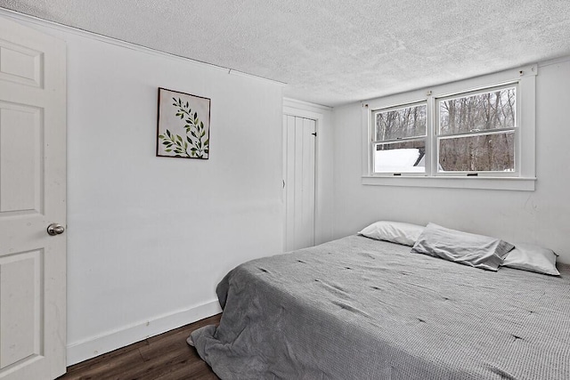 bedroom featuring a textured ceiling, dark wood-type flooring, a closet, and baseboards