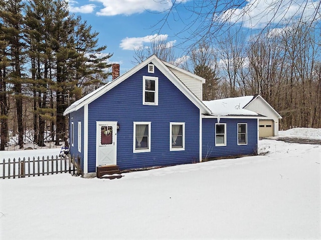 snow covered rear of property with a garage, a chimney, and fence