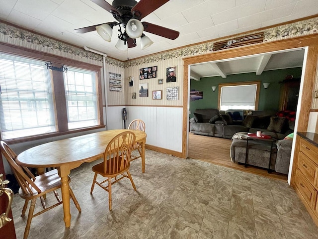 dining room with ceiling fan, wallpapered walls, wainscoting, light floors, and crown molding