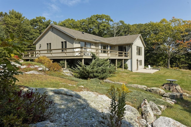 rear view of house featuring a deck, a shingled roof, a lawn, and a patio area