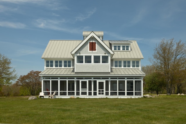 rear view of house featuring a standing seam roof, a lawn, a sunroom, and metal roof