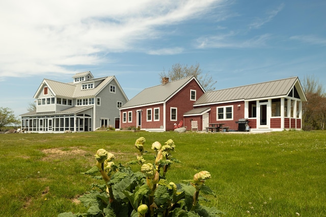 rear view of house with a yard, metal roof, a standing seam roof, and a sunroom