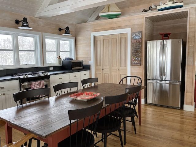 dining room featuring wood ceiling, wooden walls, vaulted ceiling with beams, and light wood-type flooring