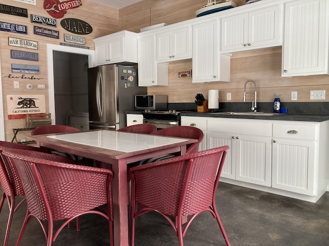 kitchen with freestanding refrigerator, a sink, white cabinets, wood walls, and dark countertops