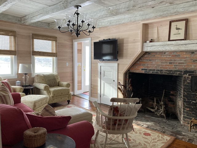 living area with wooden walls, hardwood / wood-style floors, beam ceiling, a fireplace, and an inviting chandelier