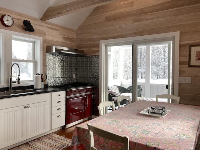 kitchen featuring dark countertops, wooden walls, extractor fan, lofted ceiling with beams, and a sink