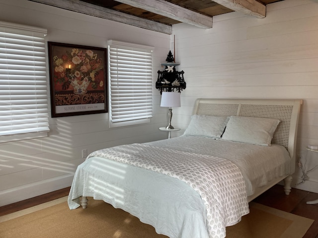 bedroom with beamed ceiling and wood finished floors