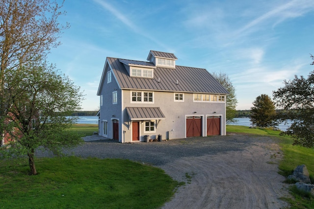 view of front facade with a water view, metal roof, driveway, an attached garage, and a standing seam roof