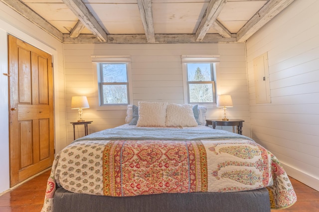 bedroom with beamed ceiling, electric panel, wood finished floors, and wood walls