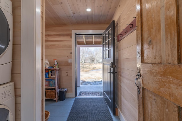 entryway featuring wooden ceiling, wooden walls, and stacked washing maching and dryer