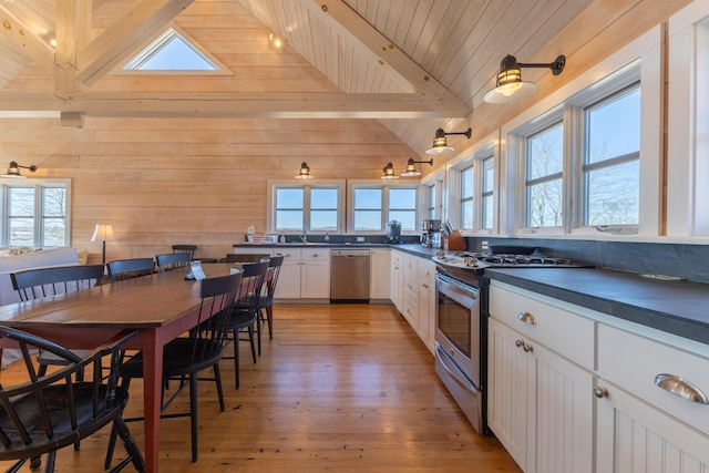 kitchen featuring light wood finished floors, lofted ceiling with beams, appliances with stainless steel finishes, white cabinetry, and dark countertops