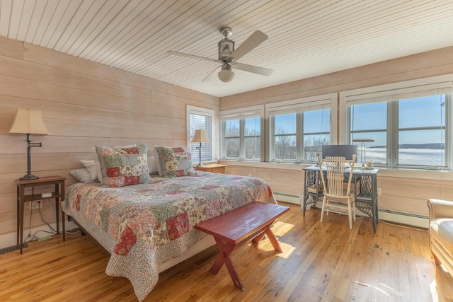 bedroom featuring wooden walls, multiple windows, a baseboard radiator, and wood finished floors