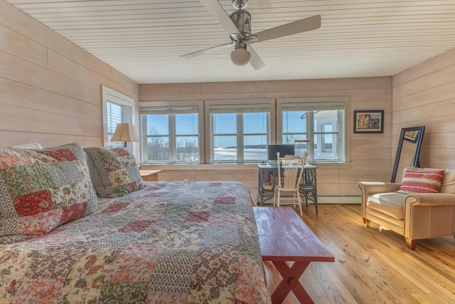 bedroom featuring a ceiling fan, wooden walls, wood finished floors, and baseboard heating