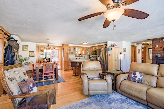 living area featuring a ceiling fan, light wood-type flooring, and a textured ceiling