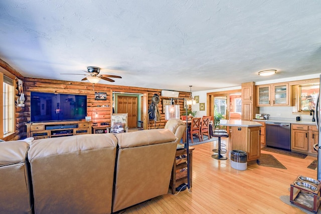 living area with light wood-type flooring, rustic walls, ceiling fan, and a textured ceiling