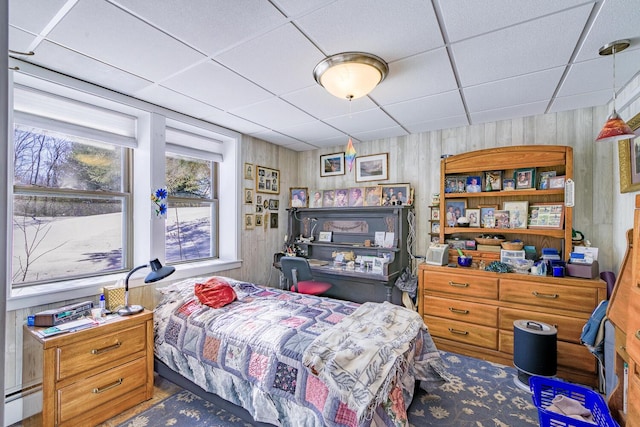 bedroom with a paneled ceiling, wood walls, and baseboard heating