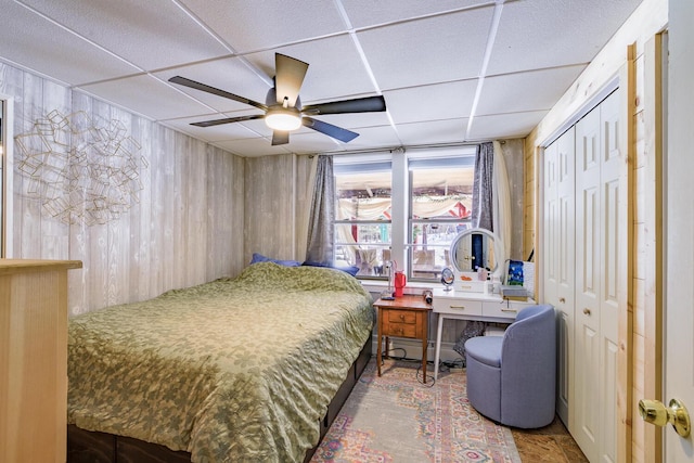 bedroom featuring a paneled ceiling, wood walls, and ceiling fan