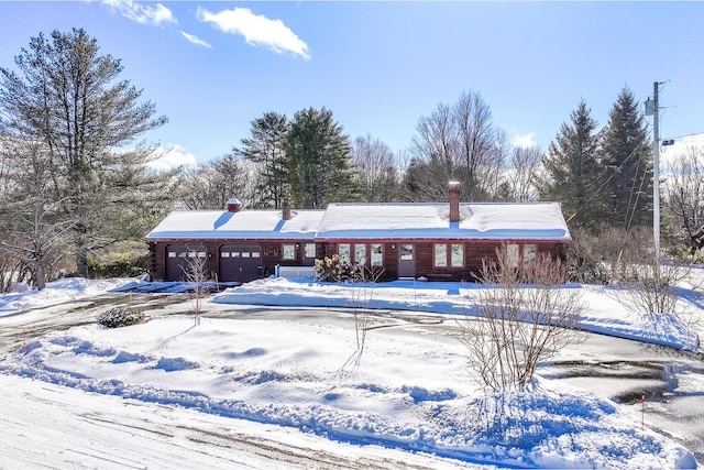 snow covered rear of property featuring an attached garage and a chimney