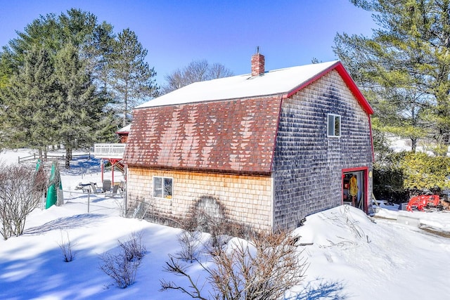 snow covered property featuring roof with shingles, a chimney, and a gambrel roof