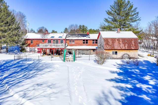 snow covered back of property with a wooden deck