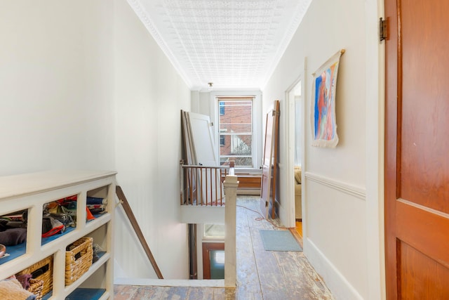 corridor featuring baseboards, wood finished floors, crown molding, and an upstairs landing