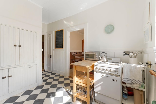 kitchen with light floors, a toaster, white electric stove, and a wainscoted wall