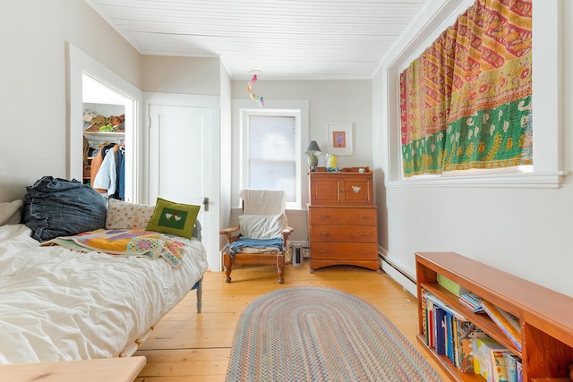 bedroom with light wood-style floors, a baseboard heating unit, and a closet