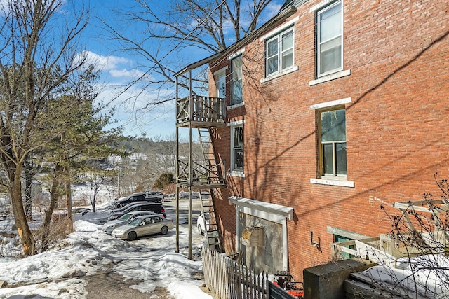 snow covered property with brick siding and a balcony