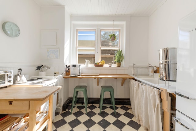 kitchen with white range with electric stovetop, a toaster, a wainscoted wall, and light floors