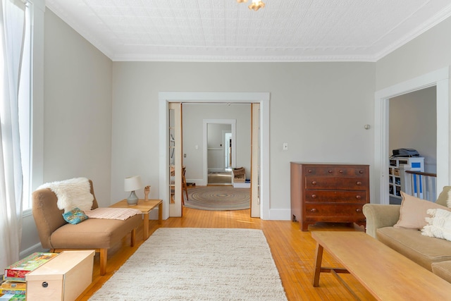 sitting room featuring light wood-style floors, baseboards, and ornamental molding