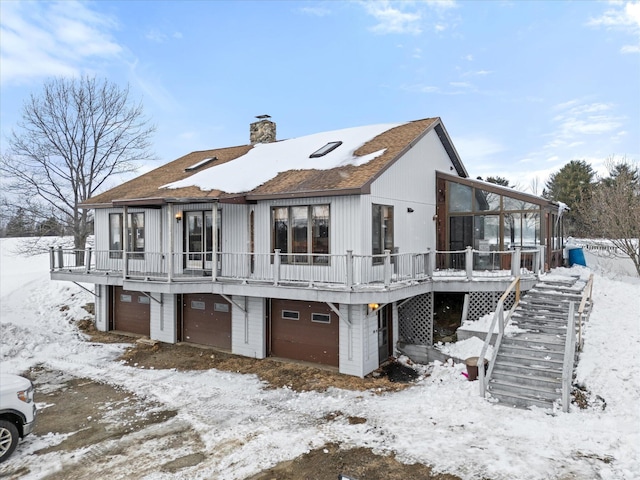 snow covered property featuring stairway, a chimney, and an attached garage