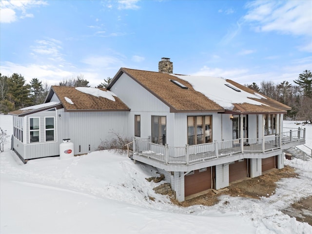 snow covered back of property featuring a garage, a shingled roof, and a chimney