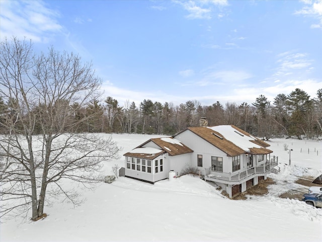 snow covered rear of property featuring a sunroom