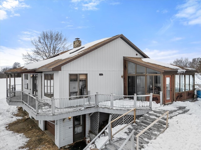 snow covered back of property with a sunroom and a chimney