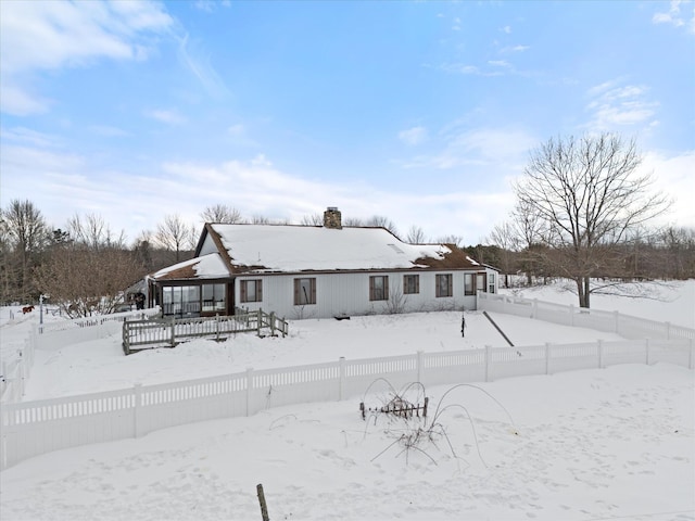 snow covered back of property featuring a chimney and fence