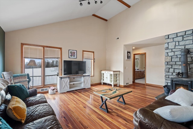 living area featuring baseboards, visible vents, wood finished floors, a wood stove, and high vaulted ceiling