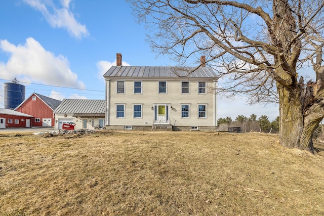 colonial inspired home with a front yard, a standing seam roof, a chimney, metal roof, and a garage