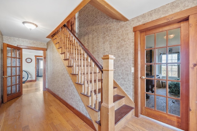 stairs with baseboards, wallpapered walls, french doors, and hardwood / wood-style flooring