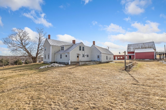 view of home's exterior with metal roof, a chimney, a standing seam roof, a lawn, and an outbuilding