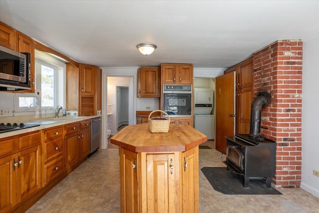 332 Back River Rd, Boothbay, ME 04537 - kitchen with butcher block countertops, black appliances, estacked washer and dryer, a center island, and brown cabinetry